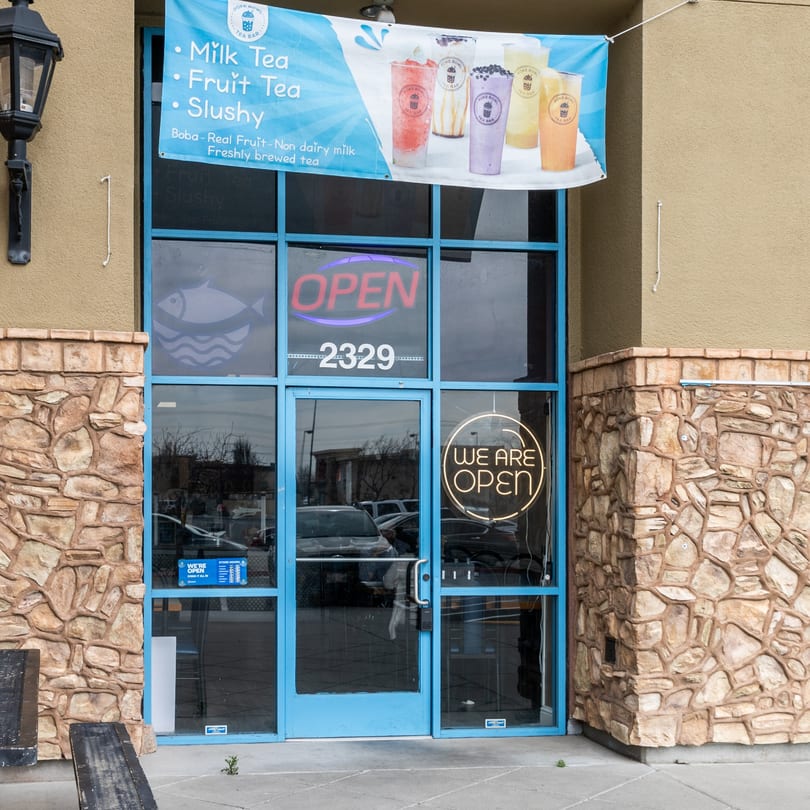 The exterior of Poke Bowl restaurant with a blue door, stone facade, and a banner advertising milk tea.