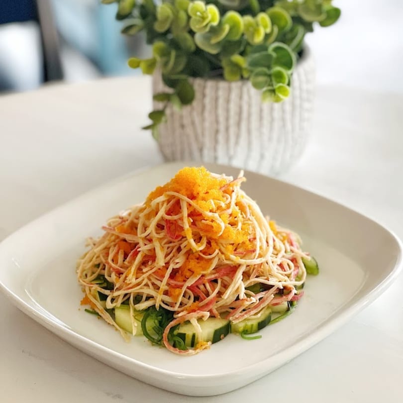 A Poke Bowl sushi salad with crab sticks, cucumber, and orange tobiko on a white plate.