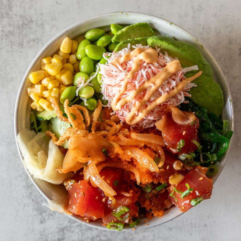 A vibrant Poke Bowl with tuna, crab, avocado, edamame, corn, and crispy onions.