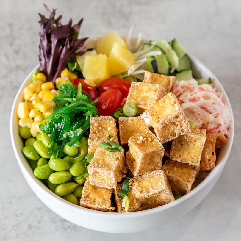 A vibrant Poke Bowl with crispy tofu, edamame, corn, seaweed, tomatoes, pineapple, and crab salad.
