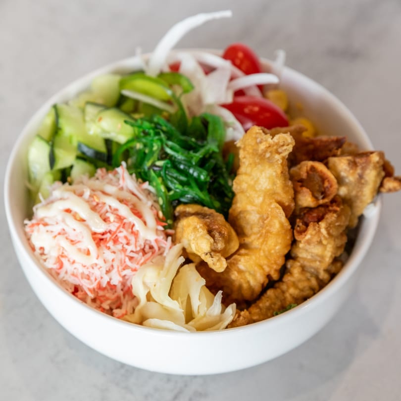 Poke Bowl with fried fish, crab salad, seaweed, cucumber, tomatoes, and pickled ginger.